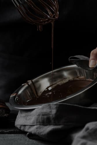 A metal bowl with liquid chocolate and a whisk